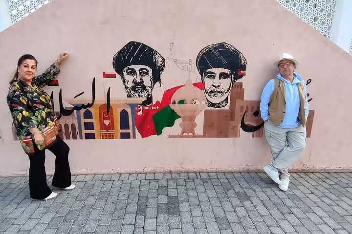 Tourists posing by colorful Muscat mural during classic sightseeing taxi tour showcasing Omani culture and heritage