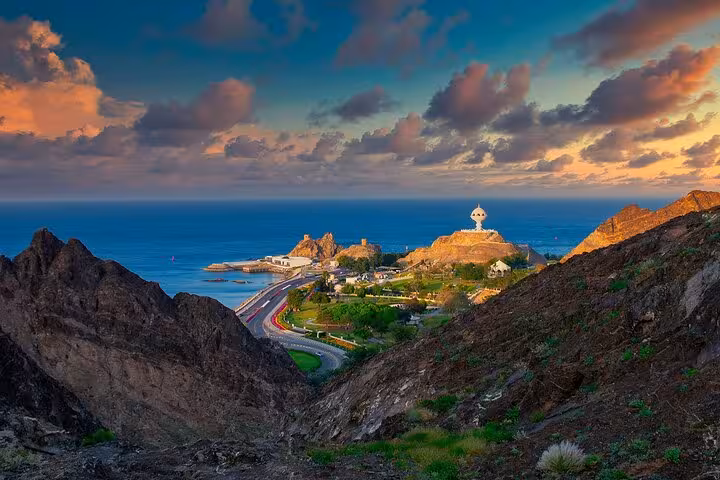 Sunset view of Muscat coastline and Riyam Monument from rocky hills on a classic private taxi sightseeing tour in Oman