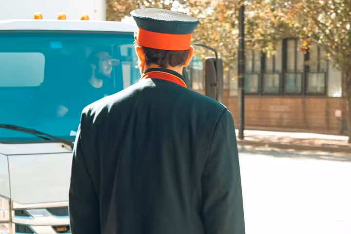 Uniformed chauffeur greeting arriving vehicle, highlighting professional pickup service for Muscat classic taxi sightseeing tours