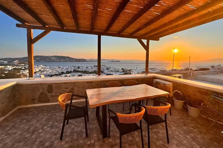 Outdoor terrace dining setup overlooking Mykonos town and Aegean sunset, ideal after cooking class experience