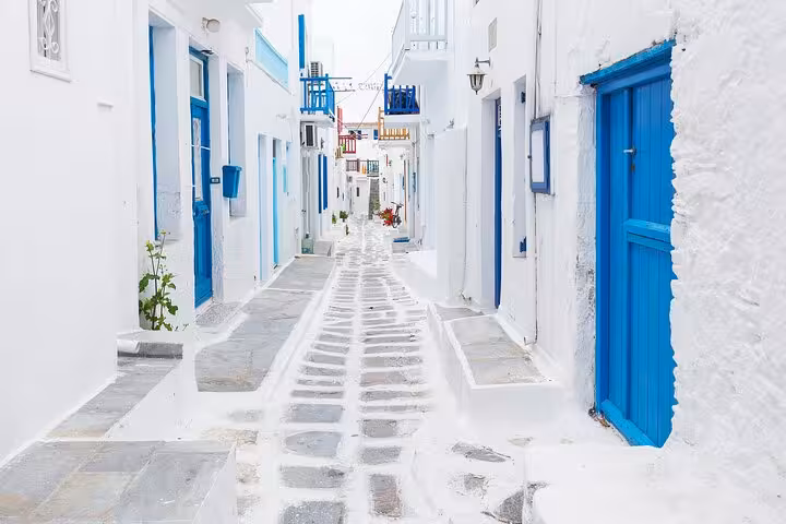 Whitewashed Mykonos alley with blue doors and balconies, 2-day tour from Athens to Santorini and Mykonos