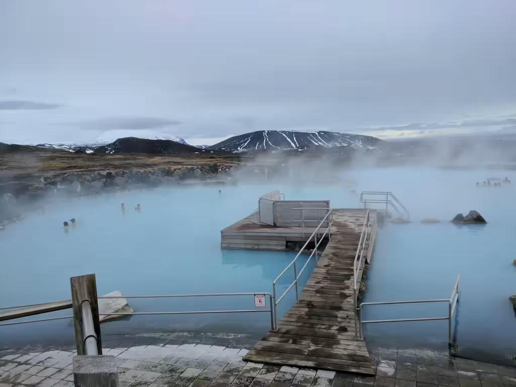 Steaming milky-blue geothermal waters of Myvatn Nature Baths with snow-capped volcanic mountains in Iceland