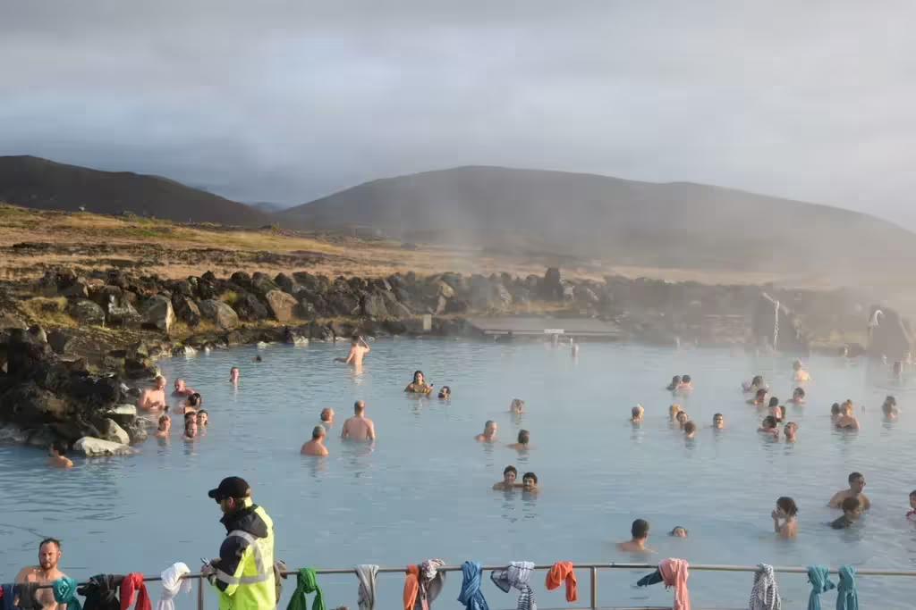 Crowds bathing in steaming blue geothermal waters at Myvatn Nature Baths with misty Icelandic mountains behind