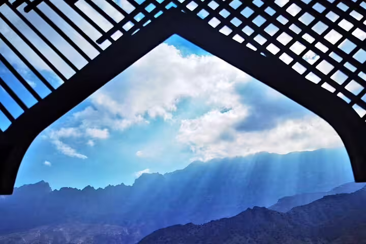 Sunlight breaking through clouds over mountains, framed by traditional architecture on a Nakhal Hotspring tour.