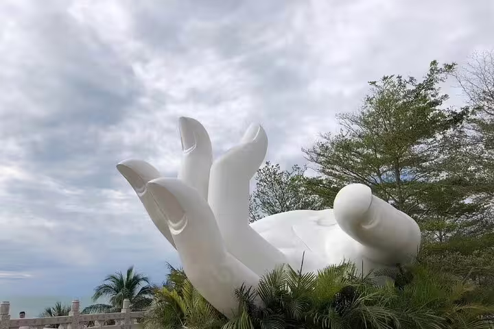 Serene view of large white Buddha hand sculpture amidst lush greenery at Nanshan Cultural Tourism Zone in Sanya.