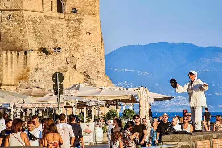 Vibrant street scene in Naples with a performer entertaining tourists near historic Castel dell'Ovo.