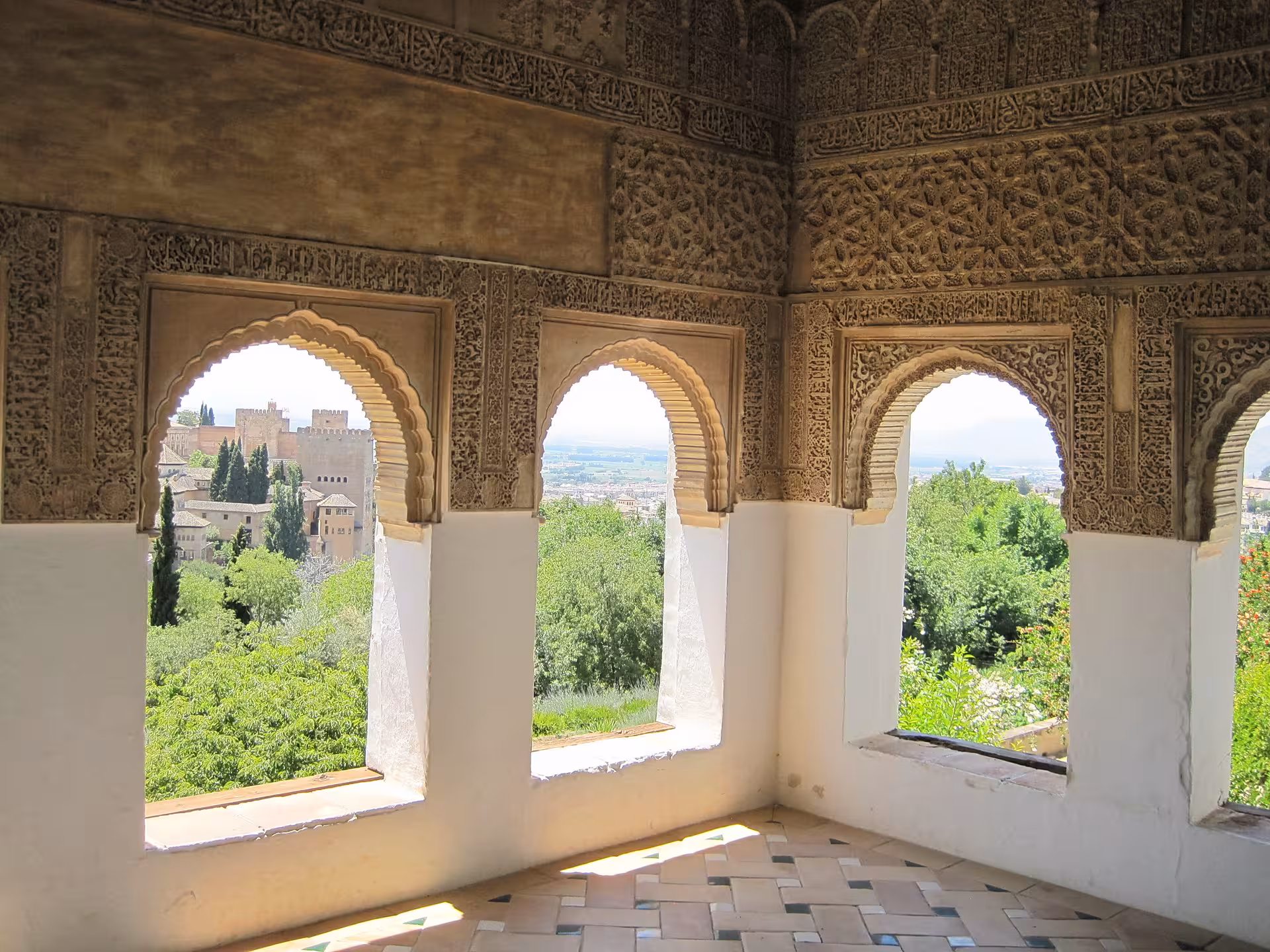 Intricate Moorish arches framing a scenic view from the Nasrid Palaces in Alhambra, Granada.