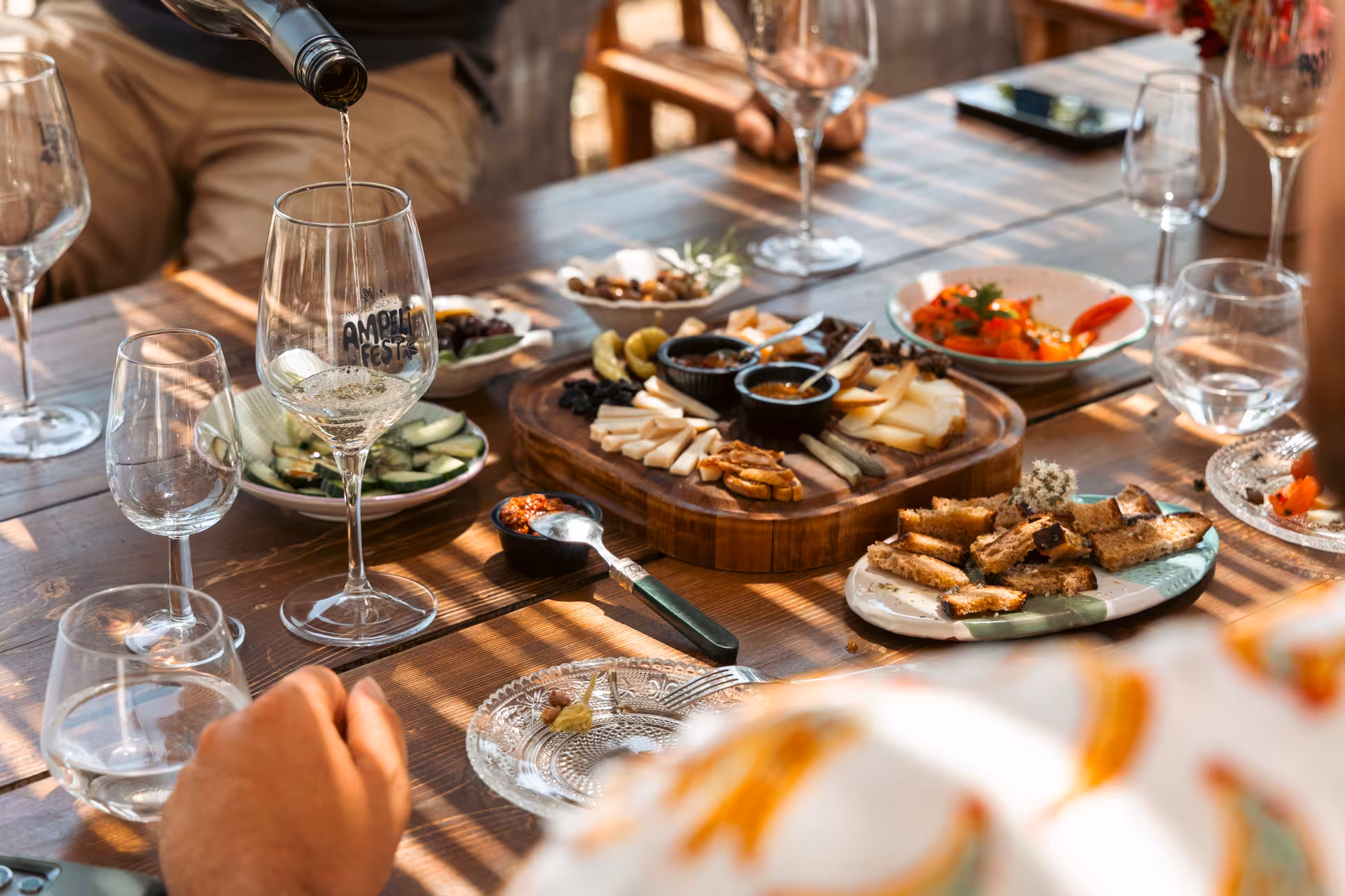 Pouring Greek white wine beside a Naxos cheese board with olives, spreads and rusks during a tasting tour
