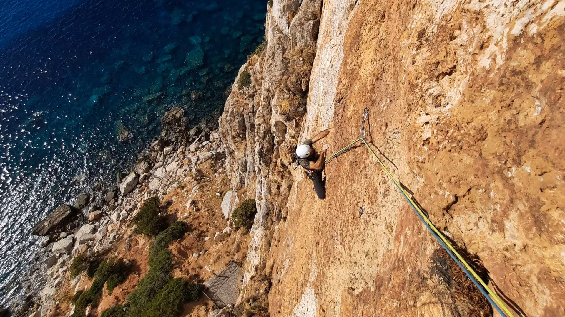 Climber scaling the rugged cliff of Masua with stunning turquoise sea view below, perfect for adventure seekers.