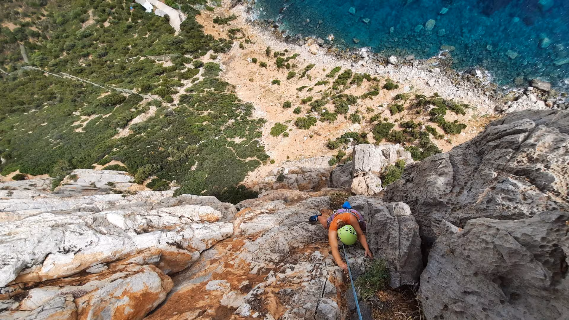 A climber ascends the steep Masua cliffside overlooking the breathtaking coastline and azure waters of Sardinia.