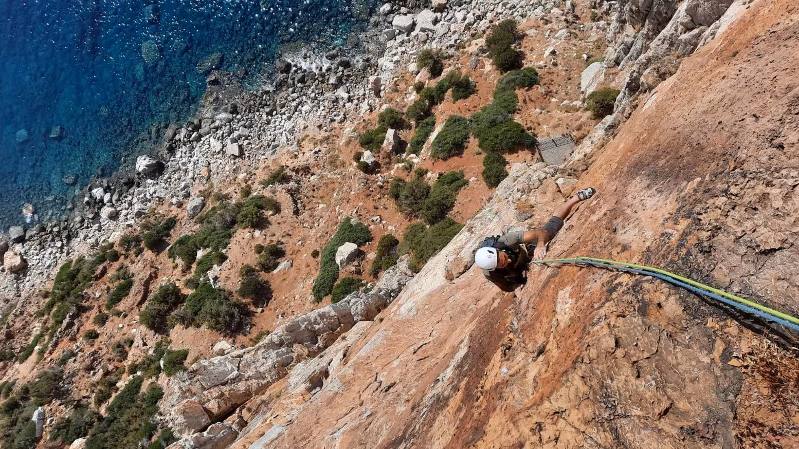Adventure seeker ascending the steep cliff face of Masua, overlooking the vibrant blue waters of Sardinia.