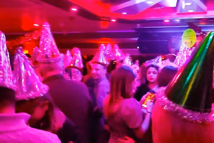 Crowded New Year's Eve party cruise Istanbul dance floor with DJ music, lights, and festive hats onboard