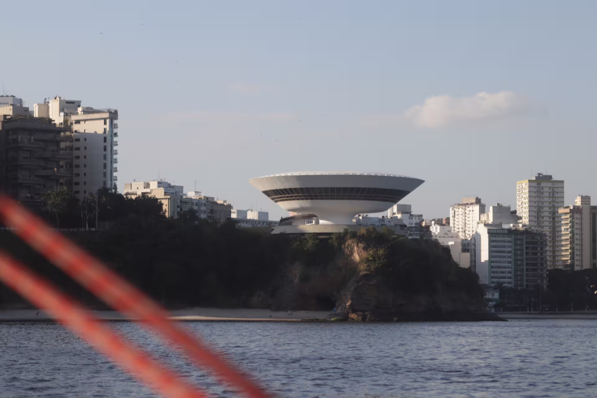 Modern architecture of Niterói Contemporary Art Museum against Rio's skyline during sunset cruise.