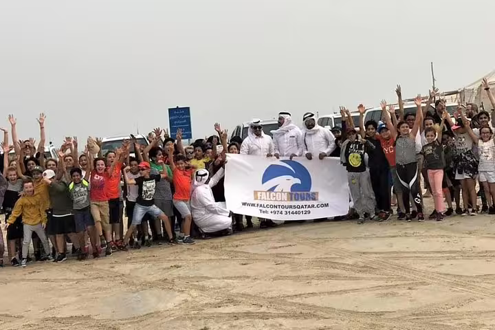 Group of tourists with guides holding a banner on a desert tour in North Qatar, showcasing cultural and adventure experiences.