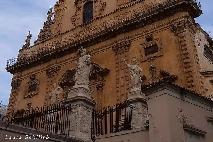 Majestic baroque facade of a historic building in Noto, adorned with detailed sculptures under a cloudy sky.