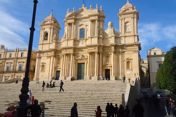 Baroque architecture of Noto Cathedral with grand stairway under a bright blue sky, ideal for Sicilian cultural tours.