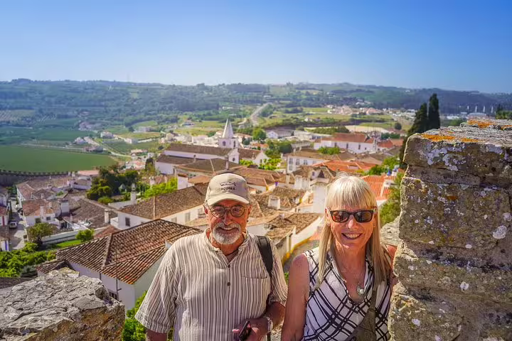 Couple enjoying scenic view of Óbidos village from the Vicentine Coast tour, showcasing historic architecture and lush landscapes.