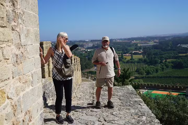 Tourists enjoying panoramic views from a historic stone walkway in Óbidos, showcasing lush landscapes and ancient architecture.