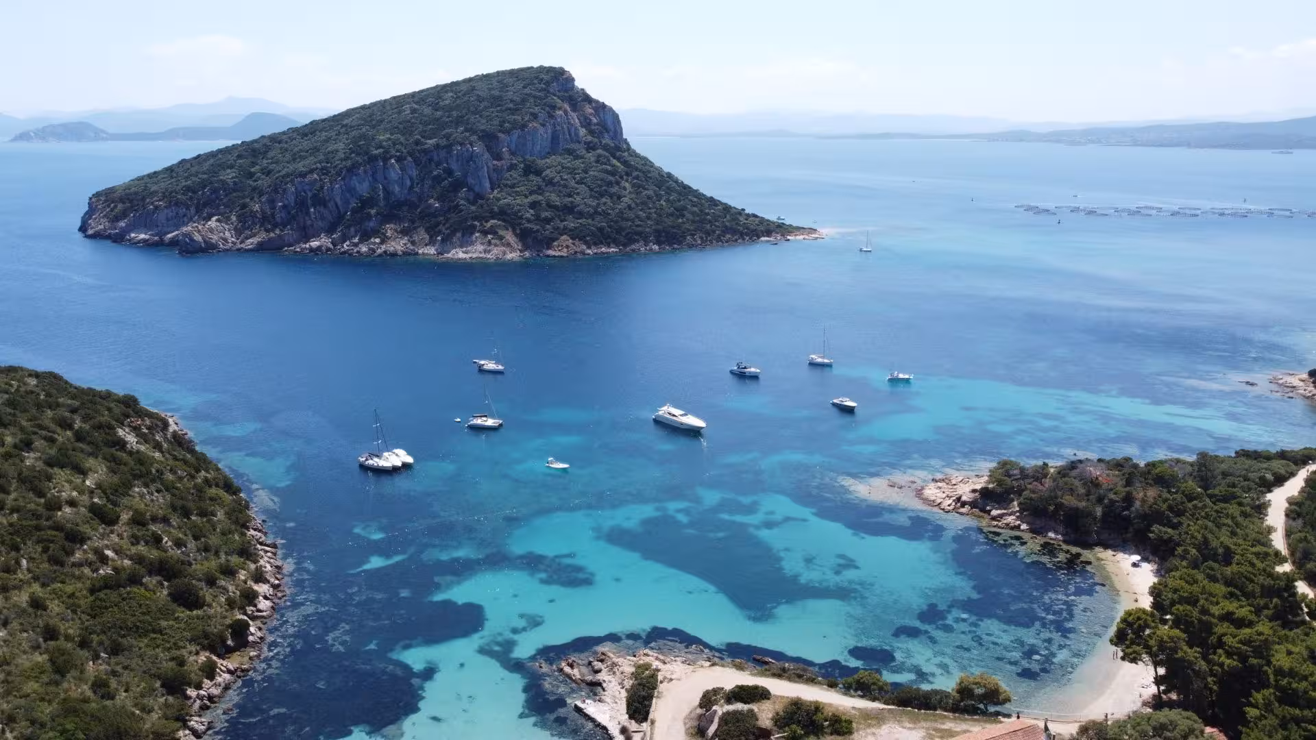 Aerial view of boats anchored near Cala Moresca, with lush greenery and crystal-clear waters in the Sardinian landscape.
