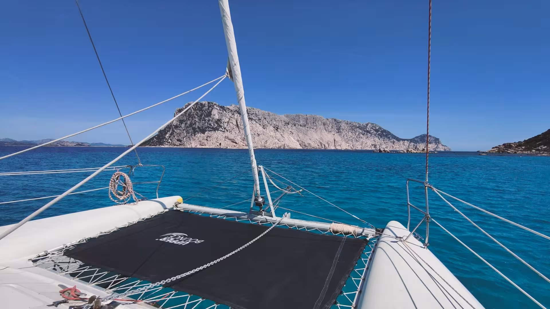 Catamaran view of Cala Moresca's turquoise waters and rugged cliffs, perfect for a scenic tour from Olbia.