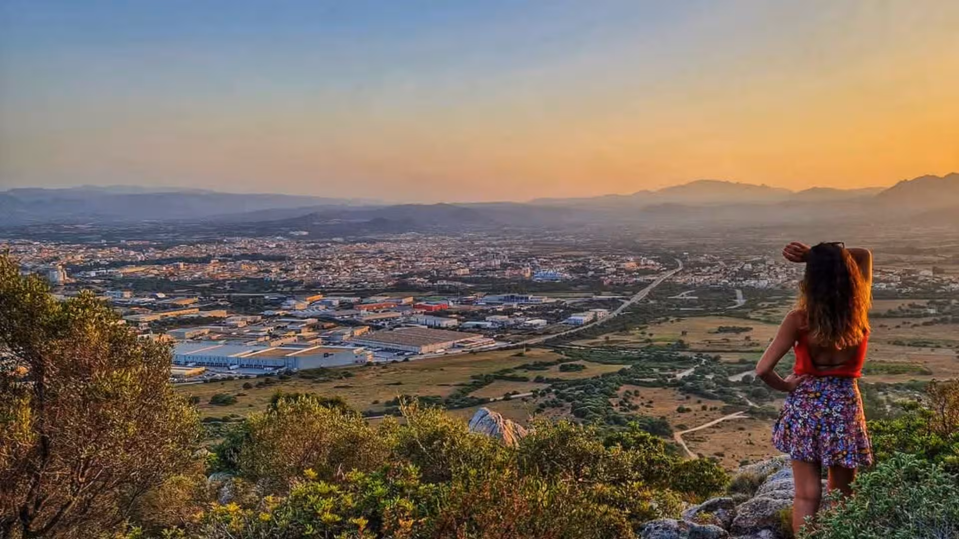 Person enjoying panoramic views of Olbia from a hilltop at sunset, showcasing the city's stunning landscape and history.
