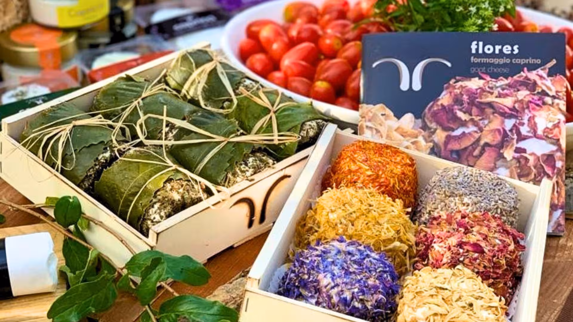 Assorted Oliena goat cheese balls with colorful edible flower coatings and fresh tomatoes, perfect for tasting tours.