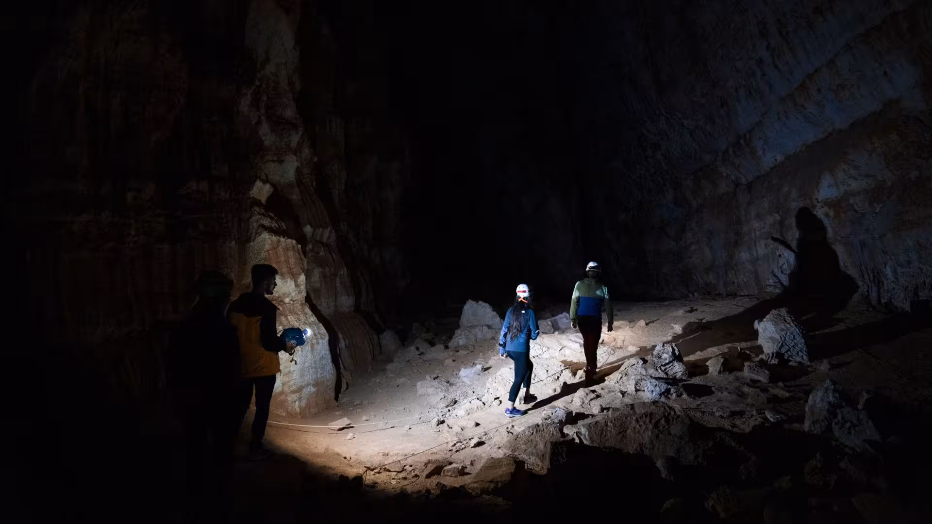 Adventurers exploring the dark interior of Sa Nurre de Su Hoda cave in Oliena with headlamps.