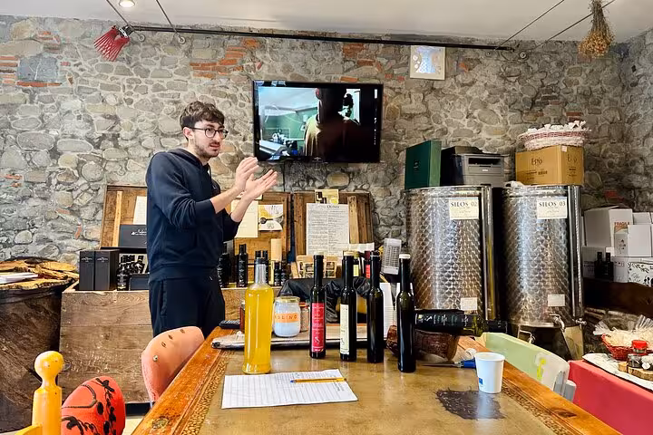 Guide explaining olive oil production process in a rustic tasting room filled with oil bottles and equipment.
