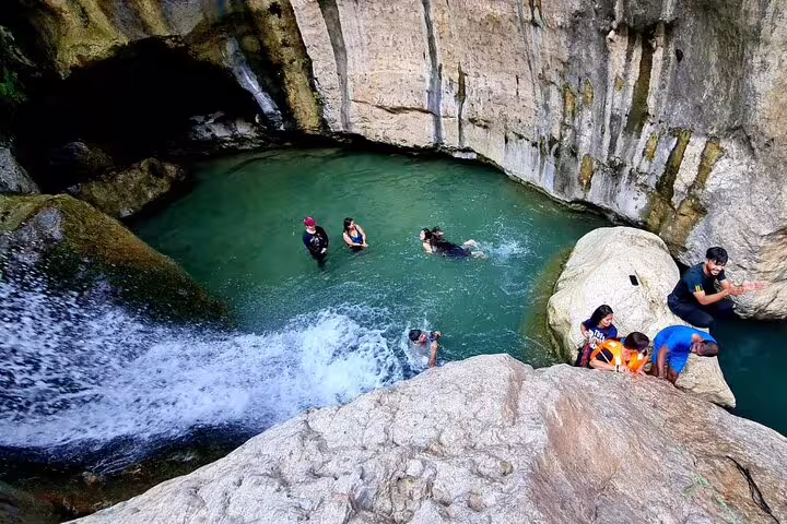 Tourists swimming and enjoying a natural pool by a waterfall in Oman's rocky canyon, perfect for a private 3-day tour.
