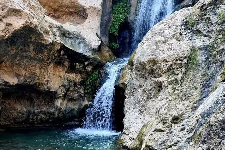 Scenic waterfall flowing into a tranquil pool surrounded by rocky cliffs, ideal for a 3-day Oman private tour adventure.