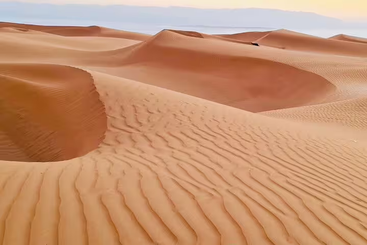 Explore the mesmerizing sand dunes of Oman, showcasing intricate patterns and sweeping desert landscapes under a clear sky.