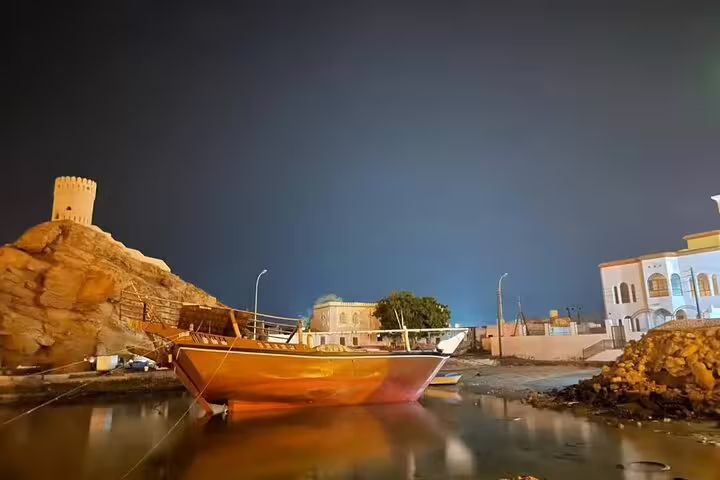 Enchanting night scene of a traditional Omani dhow by a historic fort, highlighting cultural heritage in Oman tour package.