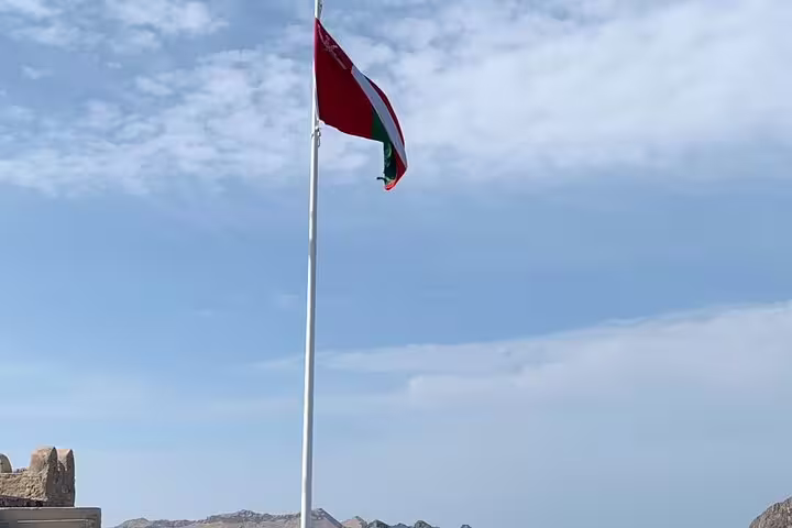 Omani flag waving against a blue sky, highlighting national pride on a private guided tour in Muscat.