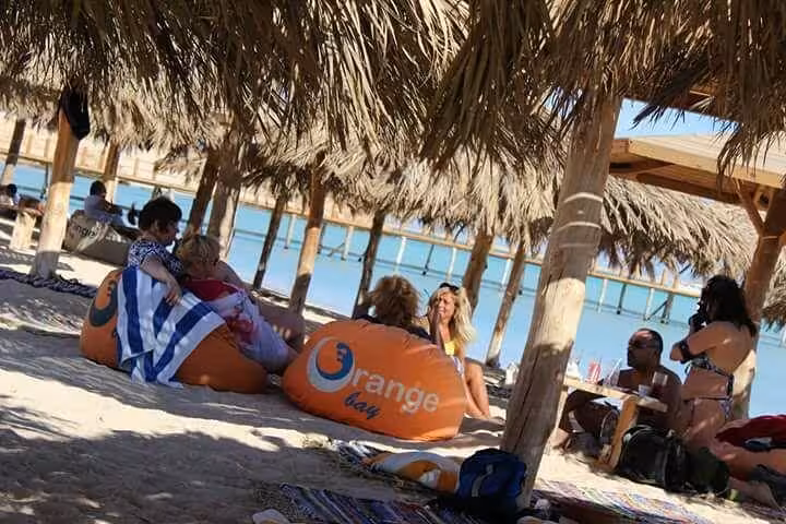 Travelers relaxing under palm huts on Orange Bay beach, Giftun Island National Park day trip from Hurghada