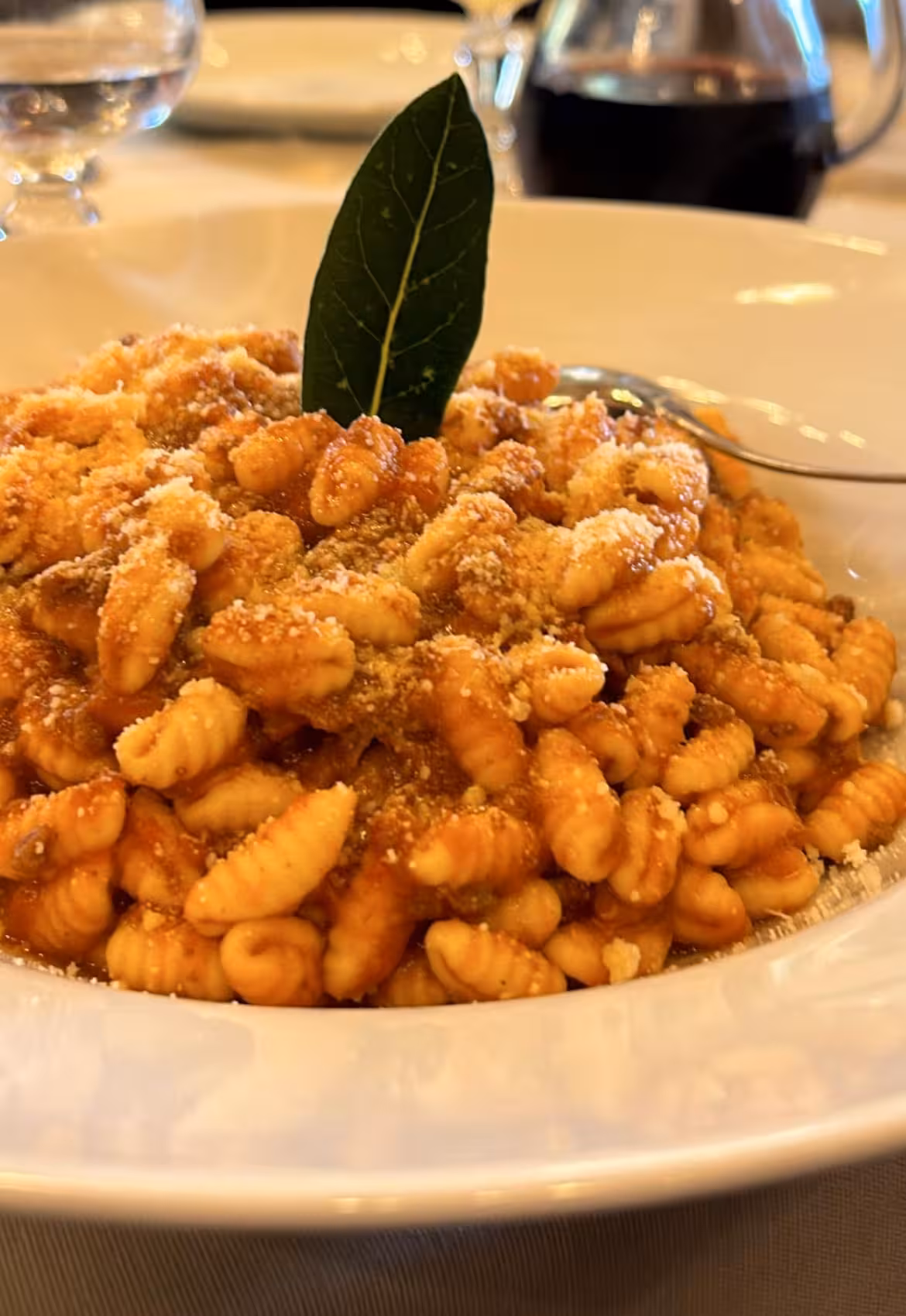 A serving of traditional Oristano pasta topped with tomato sauce, grated cheese, and garnished with a bay leaf.