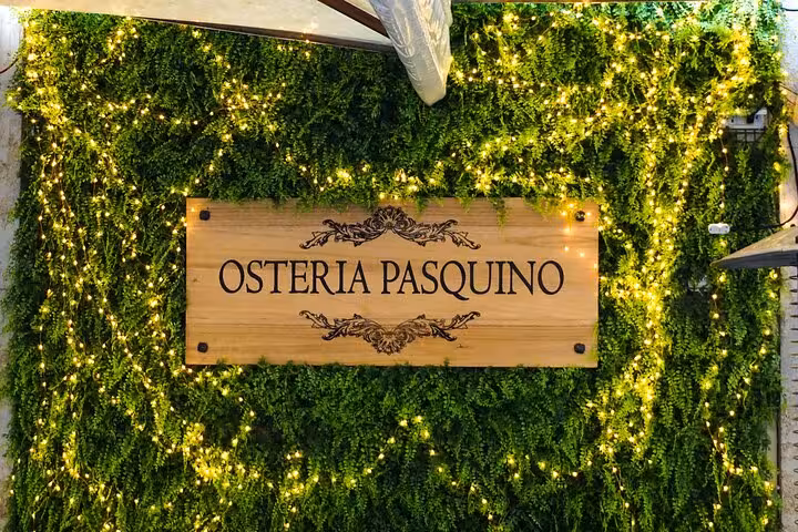Osteria Pasquino sign surrounded by greenery and lights near Piazza Navona, Rome.