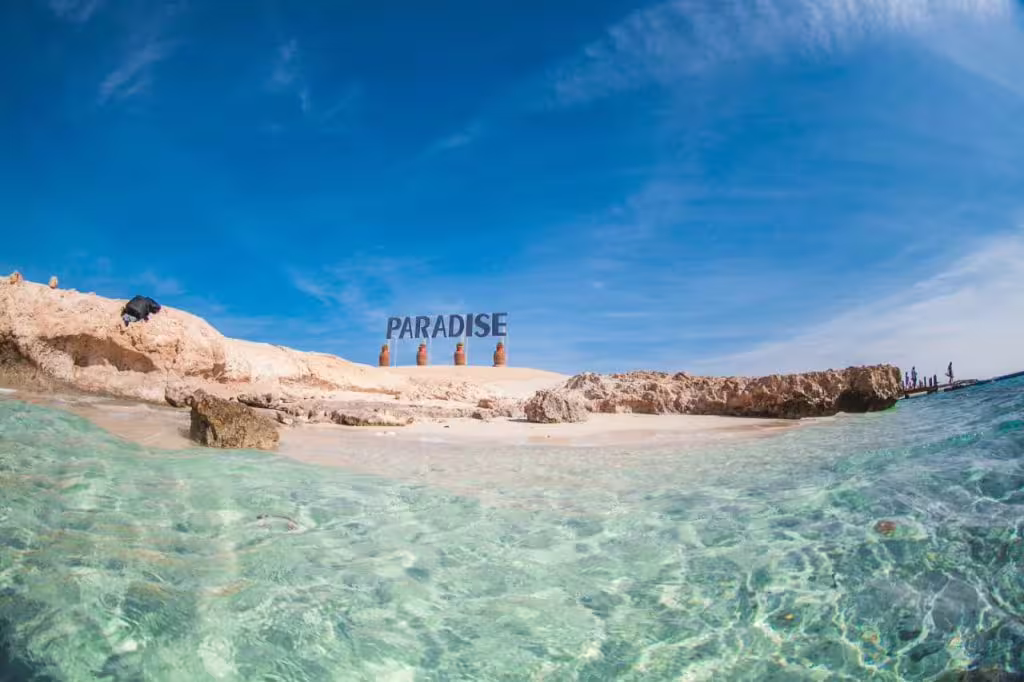 Crystal-clear lagoon and sandy beach by the Paradise Island sign, perfect for a day trip and swim