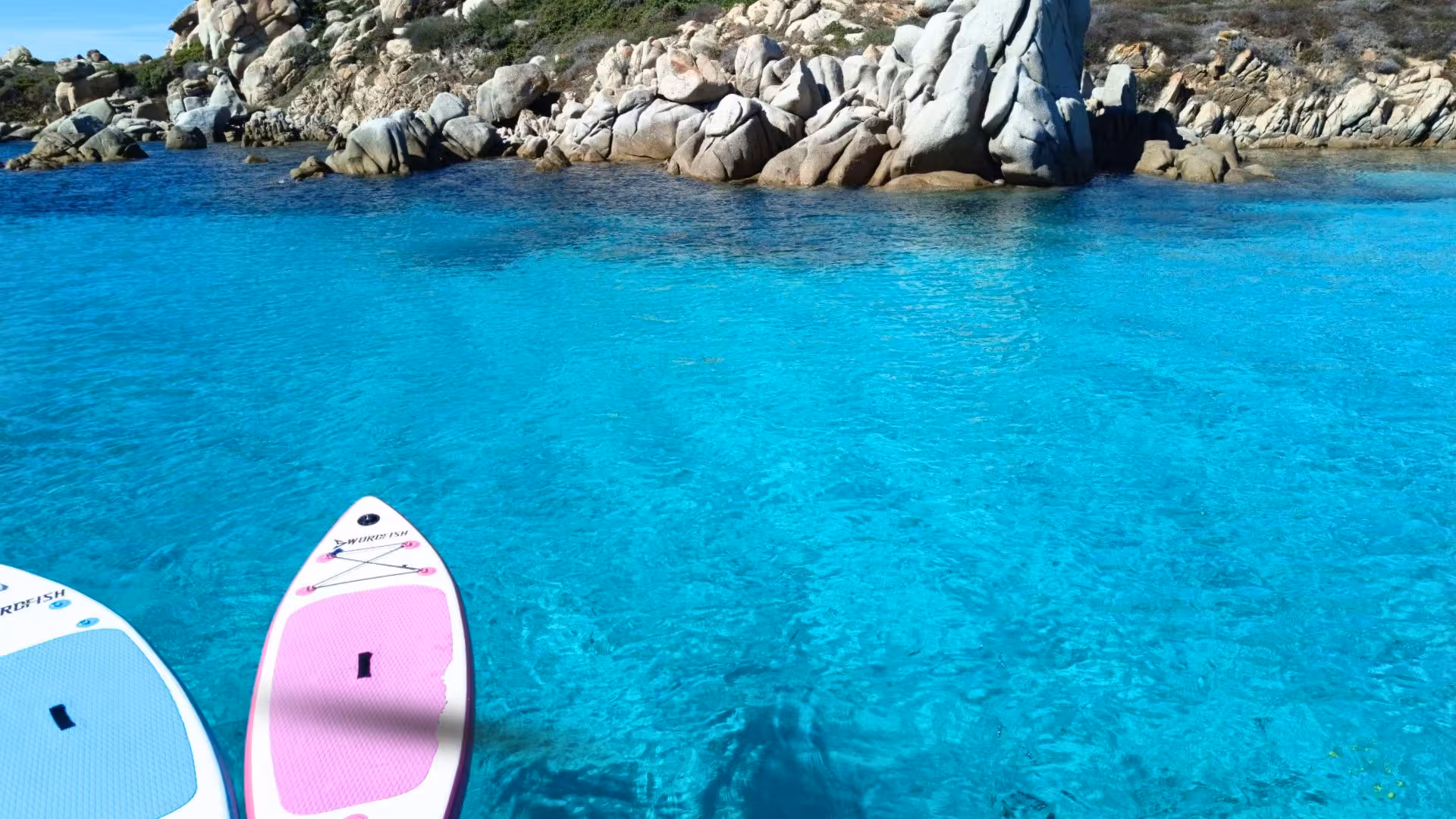 Two paddleboards floating on crystal-clear waters near rocky shores, showcasing the beauty of southern Corsica's coastline.