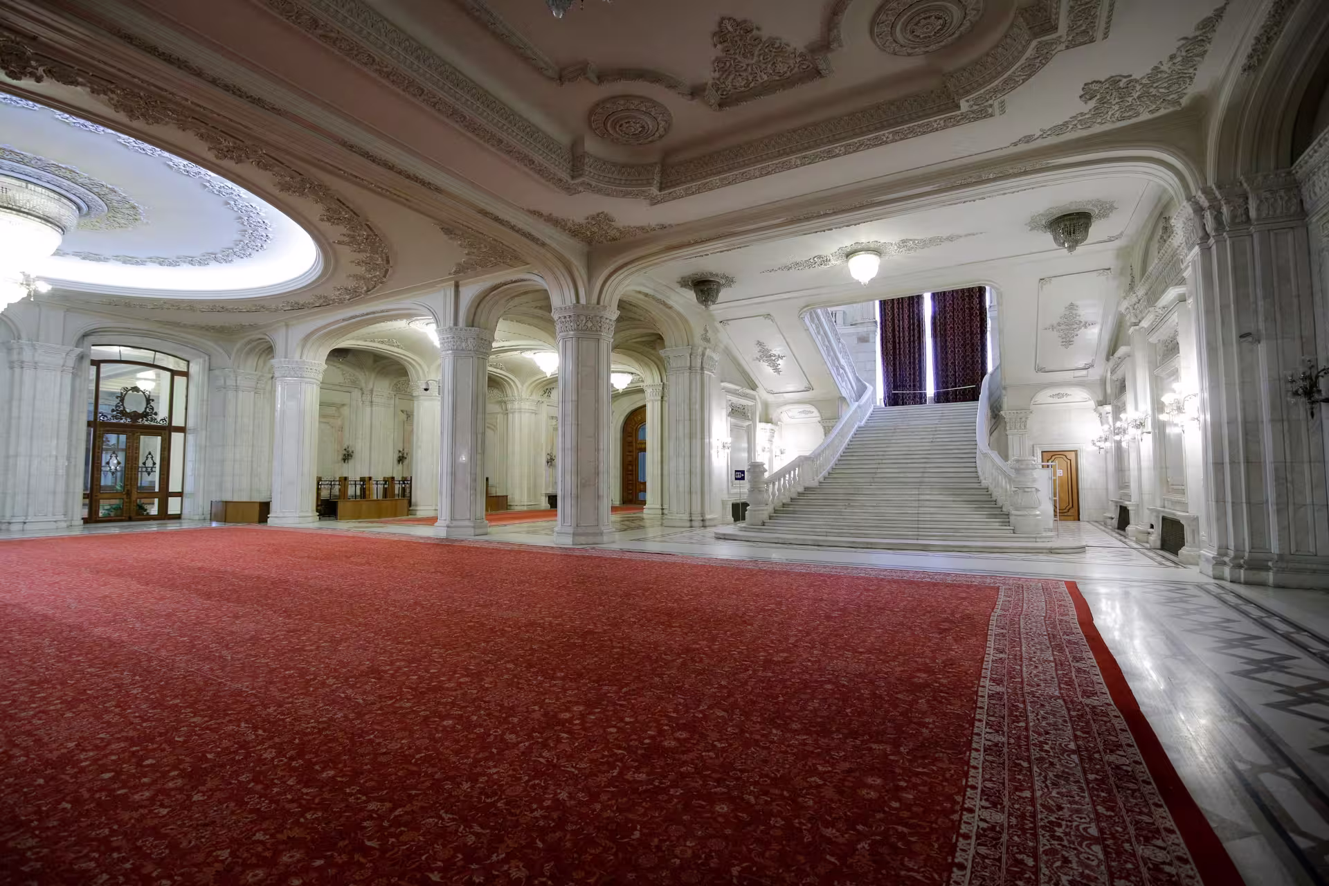 Elegant staircase and red carpeted hall inside Palace of Parliament in Bucharest, featured in Spanish guided tours.