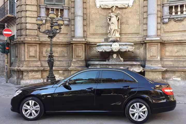 Executive black sedan parked by historic Palermo landmark, used for private transfer between Palermo Airport and Hotel Elite