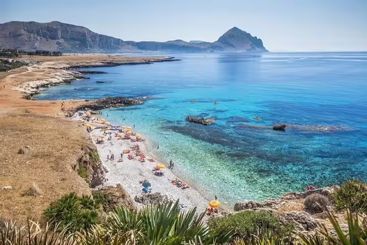 Scenic coastal view of San Vito Lo Capo with turquoise sea, pebble beach and umbrellas reached by Palermo Airport private transfer