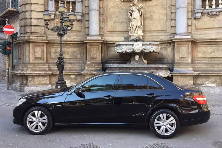 Luxury black sedan waiting by historic Quattro Canti fountain in Palermo for private 4-hour cruise passenger city tour