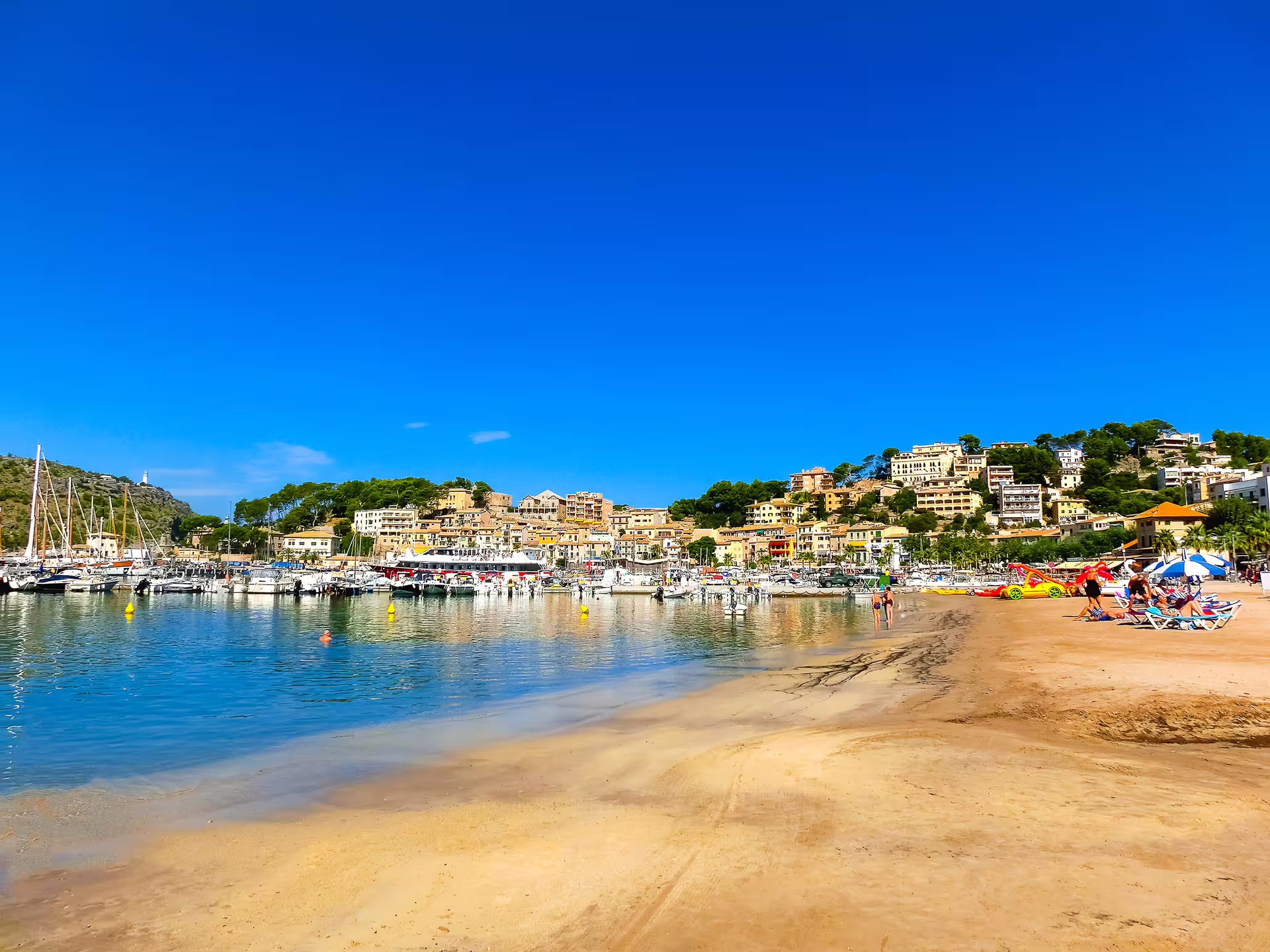Sunny Mallorca beach by Port de Sóller style marina and hillside town, scenic stop for Palma day audioguide