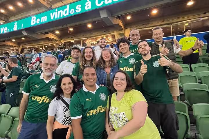 Group of Palmeiras fans smiling in São Paulo stadium stands, locals hosting travelers on soccer game tour