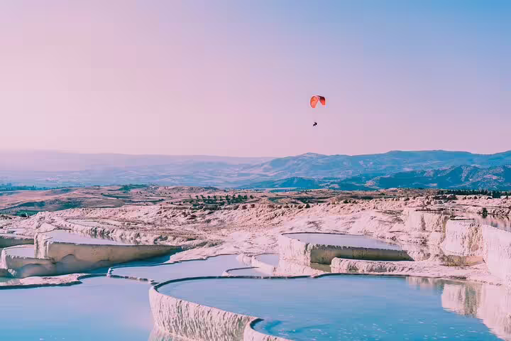Experience paragliding over Pamukkale's travertine pools with stunning mountain views on a small group tour from Izmir.