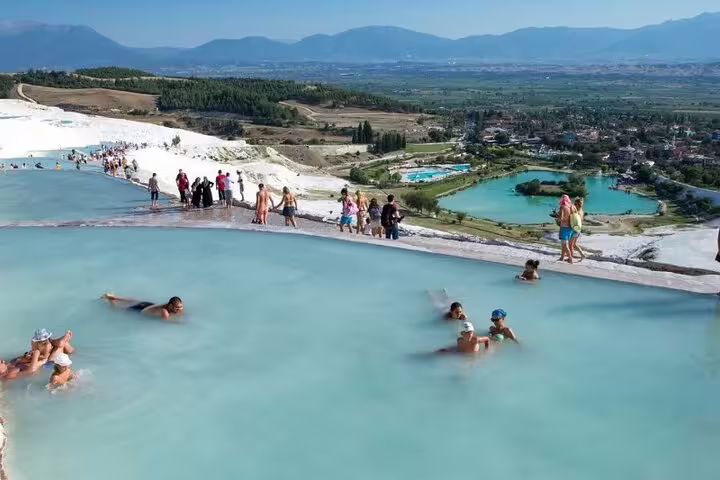 Visitors enjoying the warm thermal pools of Pamukkale with panoramic views of the surrounding landscape on a sunny day.