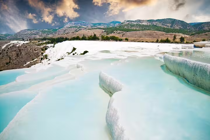 Scenic view of Pamukkale's travertine terraces with turquoise thermal waters against a dramatic sky.