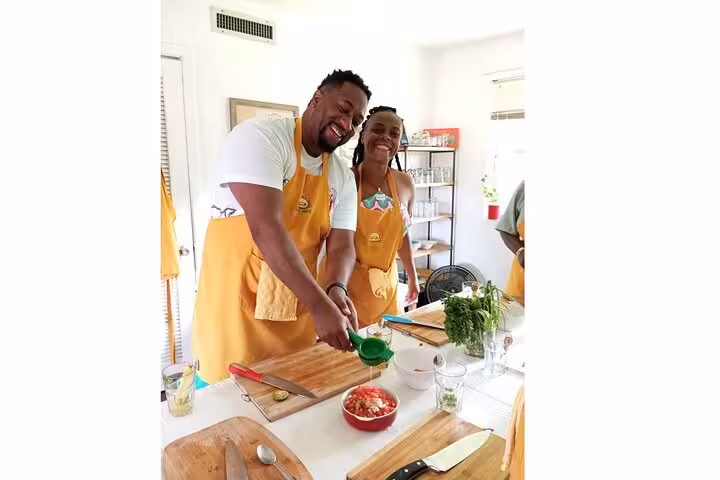 Participants in a Panamanian cooking class smiling and preparing fresh ingredients at a kitchen workstation.