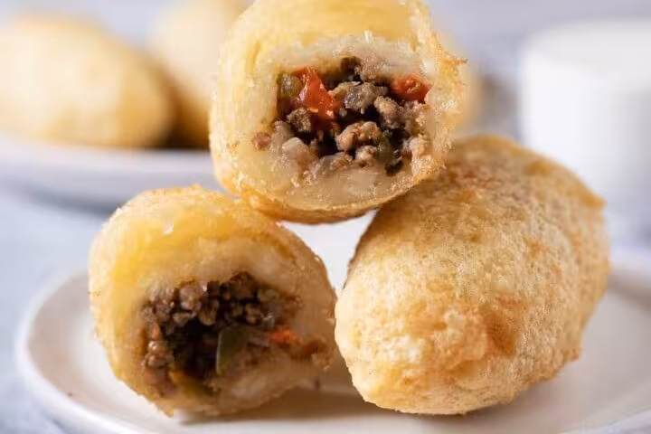 Close-up of savory Panamanian carimañolas with a crispy golden crust and seasoned meat filling on a white plate.