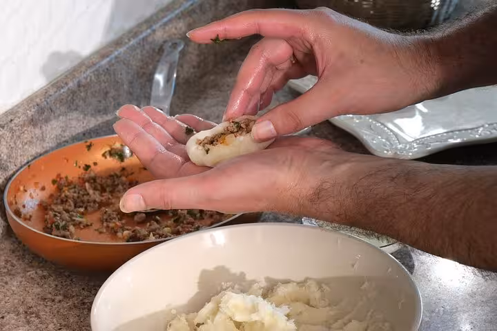 Hands shaping traditional Panamanian dish with seasoned filling, showcased in a hands-on boozy cooking class.